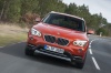 Picture of a driving 2014 BMW X1 in Valencia Orange Metallic from a frontal perspective
