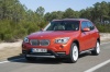 Picture of a driving 2014 BMW X1 in Valencia Orange Metallic from a front left perspective