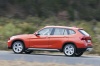 Picture of a driving 2014 BMW X1 in Valencia Orange Metallic from a rear left three-quarter perspective