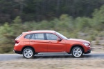 Picture of a driving 2014 BMW X1 in Valencia Orange Metallic from a right side perspective