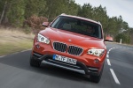 Picture of a driving 2015 BMW X1 in Valencia Orange Metallic from a frontal perspective