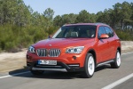 Picture of a driving 2015 BMW X1 in Valencia Orange Metallic from a front left perspective