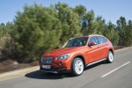 Picture of a driving 2015 BMW X1 in Valencia Orange Metallic from a front left three-quarter perspective
