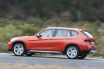 Picture of a driving 2015 BMW X1 in Valencia Orange Metallic from a rear left three-quarter perspective