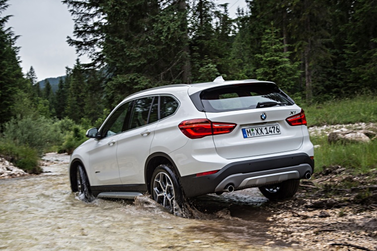 Picture of a driving 2016 BMW X1 xDrive28i in Alpine White from a rear left three-quarter perspective