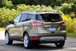 Picture of a driving 2014 Ford Escape Titanium 4WD in Ginger Ale Metallic from a rear left perspective
