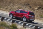 Picture of a driving 2018 Ford Escape Titanium in Ruby Red Metallic Tinted Clearcoat from a rear left three-quarter perspective
