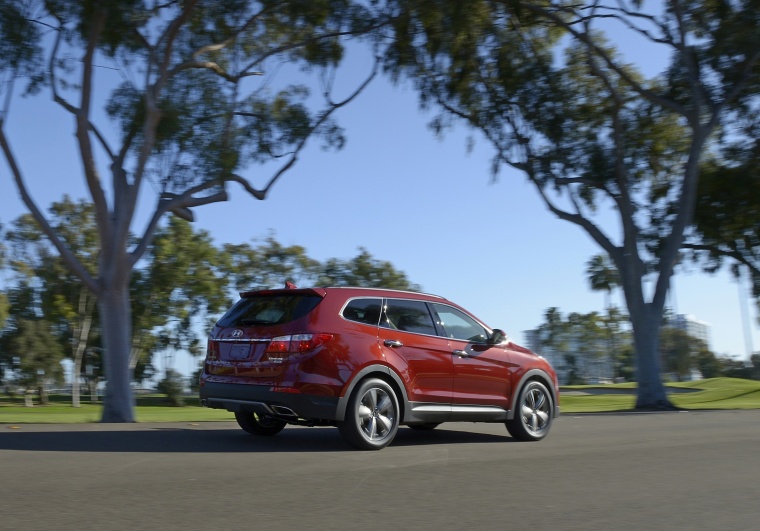 Picture of a driving 2014 Hyundai Santa Fe in Regal Red Pearl from a rear right three-quarter perspective