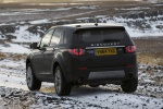 Picture of a driving 2015 Land Rover Discovery Sport HSE Luxury in Kaikoura Stone Metallic from a rear left perspective