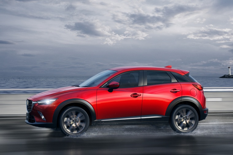 Picture of a driving 2016 Mazda CX-3 in Soul Red Metallic from a side perspective
